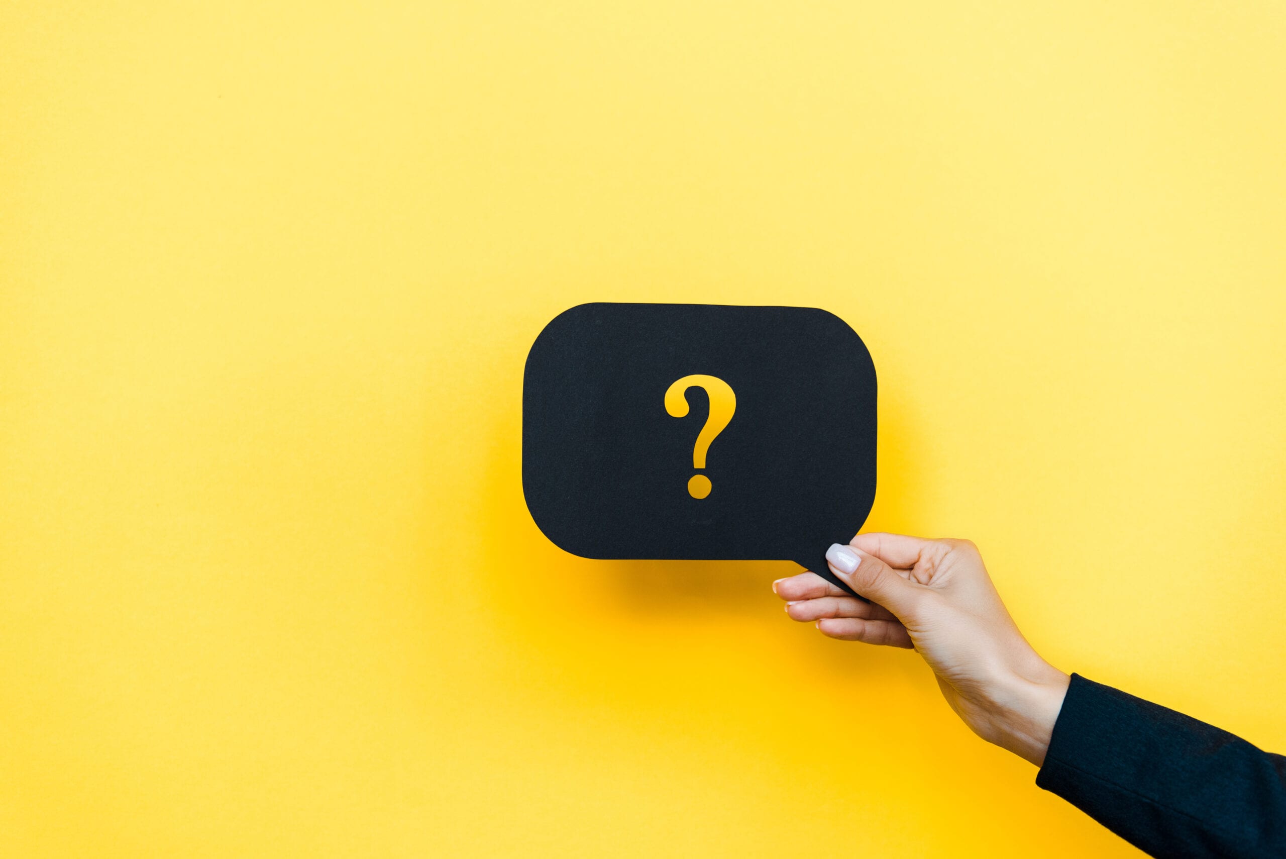 A hand holding a black speech bubble with a yellow question mark against a vibrant yellow background, symbolizing customer inquiries and support.