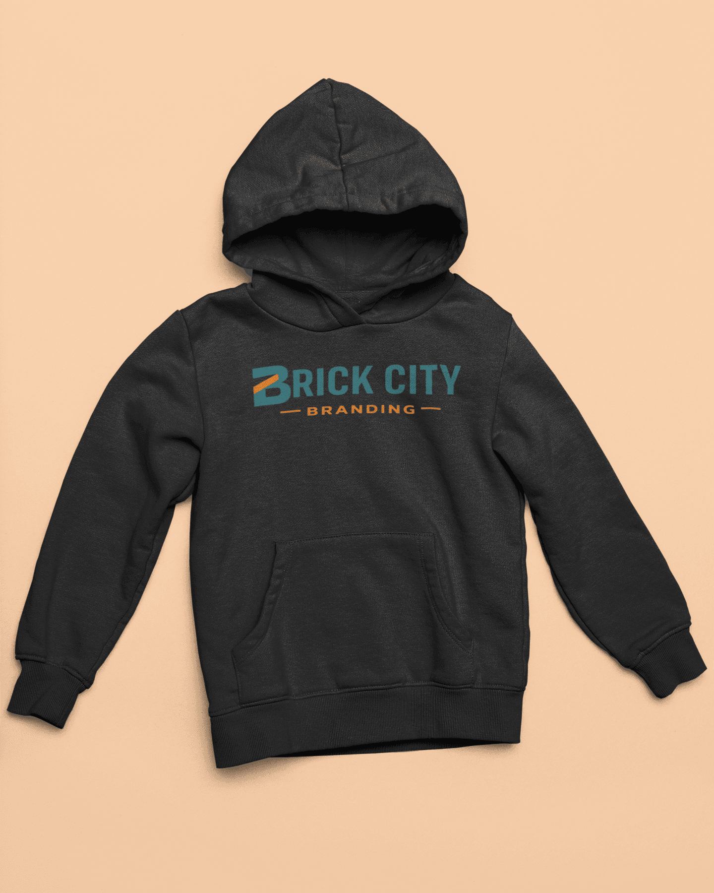 A charcoal grey pullover hoodie featuring the Brick City Branding logo centered on the chest, laid flat on a tan-colored background.