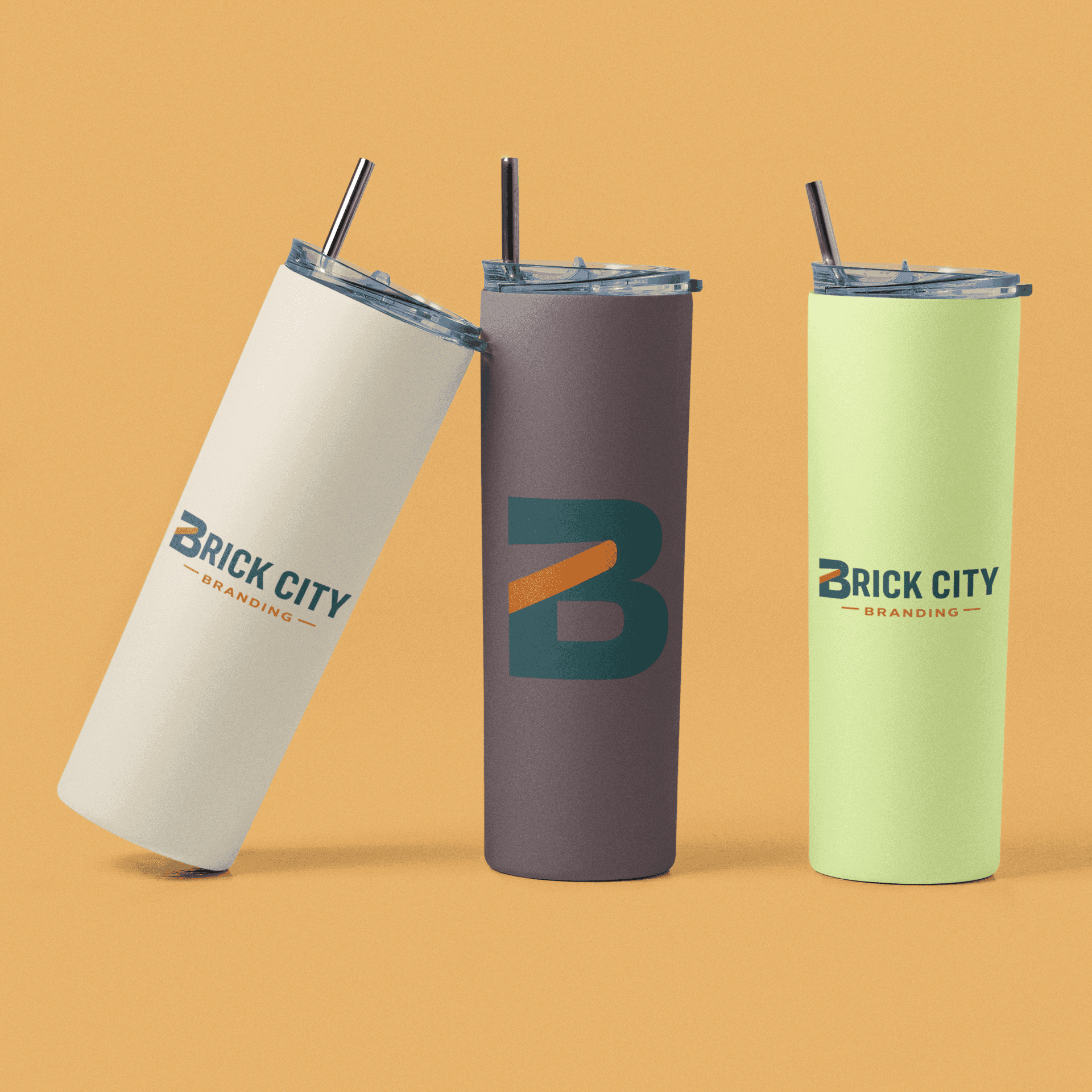Three insulated skinny tumblers in cream, mauve, and lime green featuring the Brick City Branding logo, shown with stainless steel straws on a tan background.