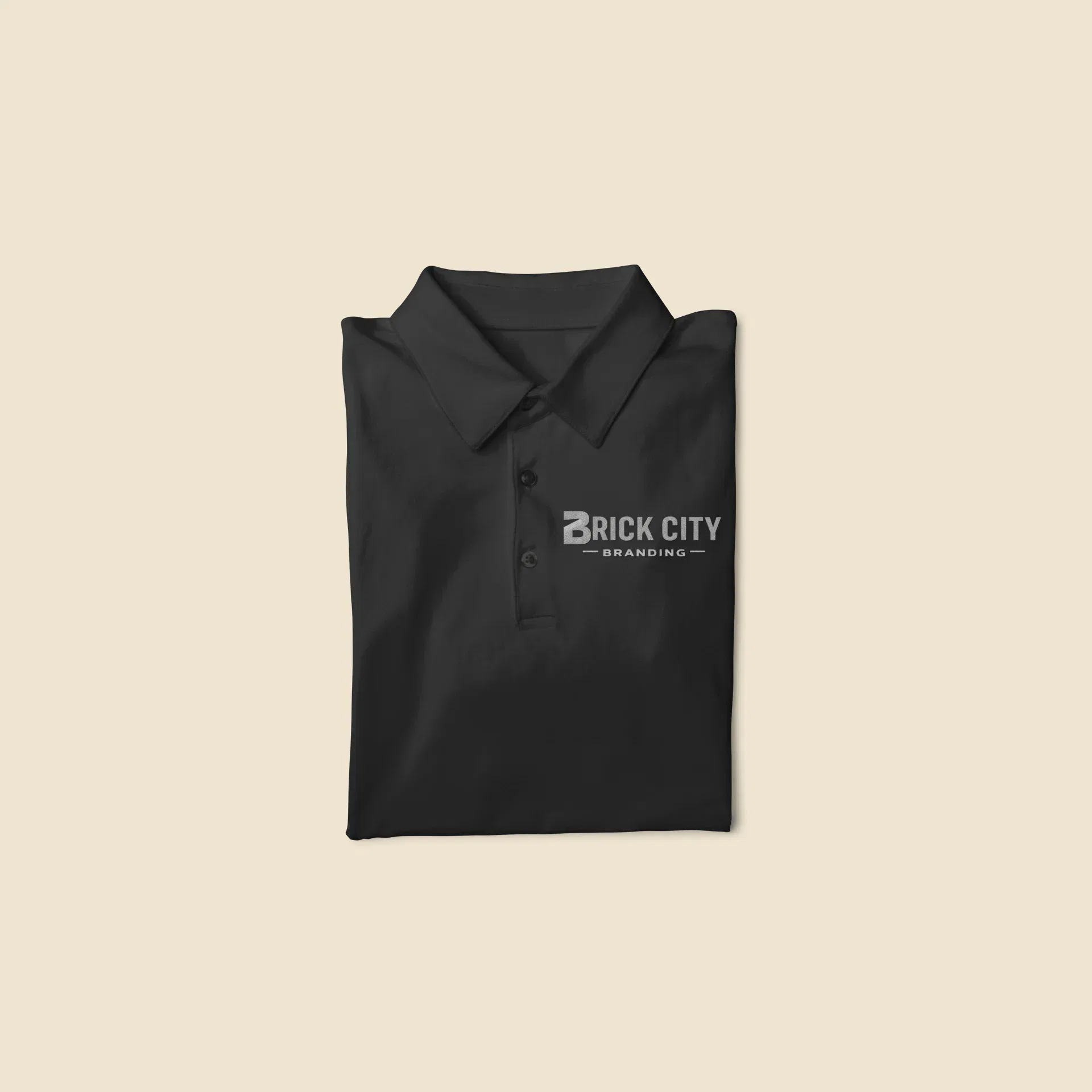A neatly folded black polo shirt featuring a single-color silver or grey embroidered 