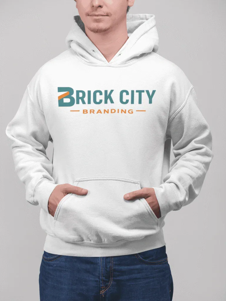 A man with a beard and glasses wearing a white knit beanie with the Brick City Branding logo, posing in front of a rustic wooden barn or cabin.