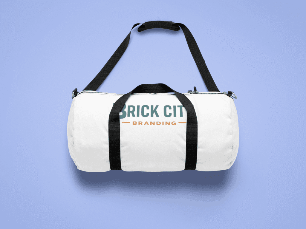 A white canvas cylindrical duffel bag with black straps featuring the Brick City Branding logo on the side, isolated on a lavender-blue background.