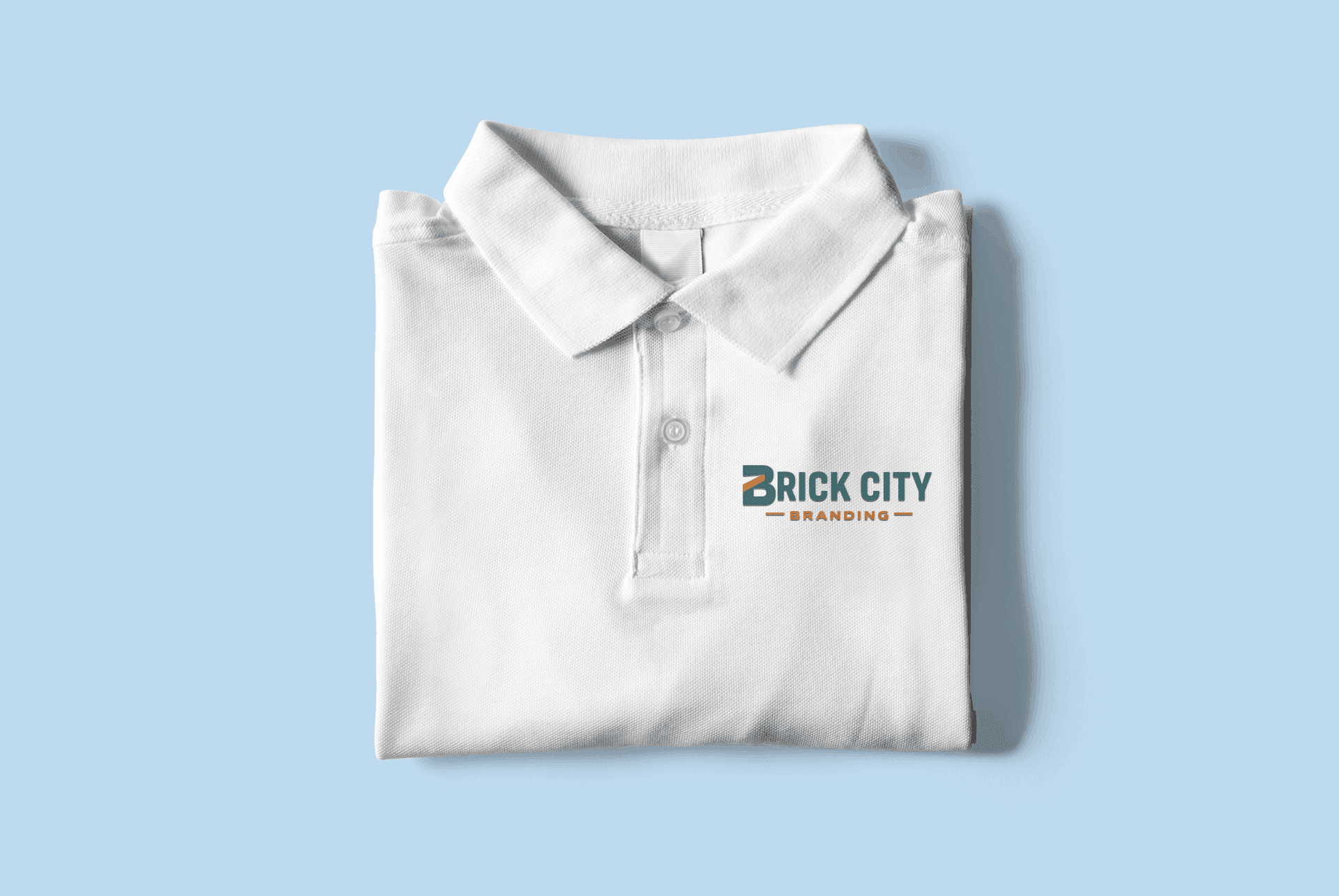 A top-down view of a folded white polo shirt showing the professional left-chest logo placement for Brick City Branding in teal and orange.