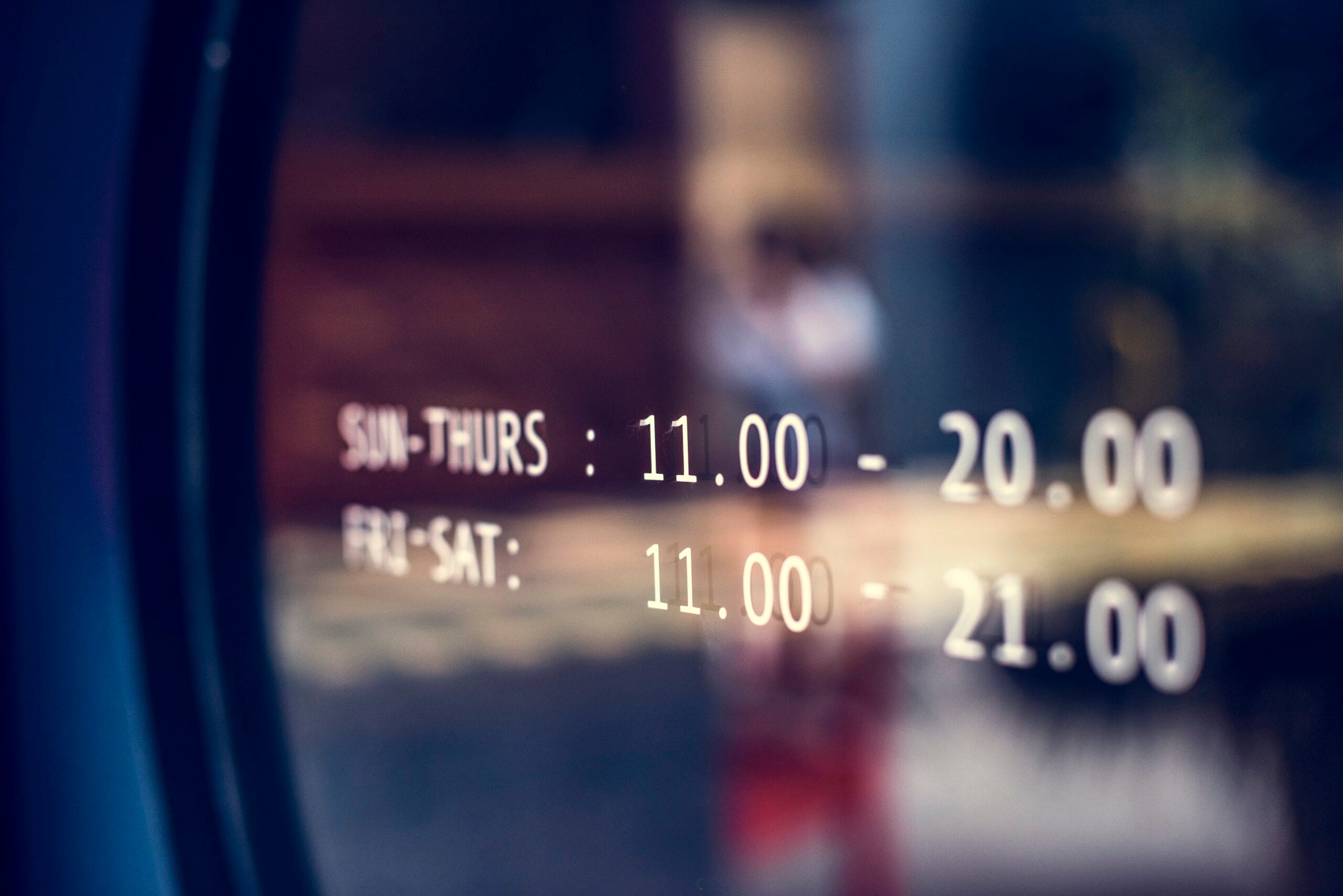 Close-up of white vinyl business hours printed on a glass door, showing operating times from 11:00 to 20:00 and 21:00.