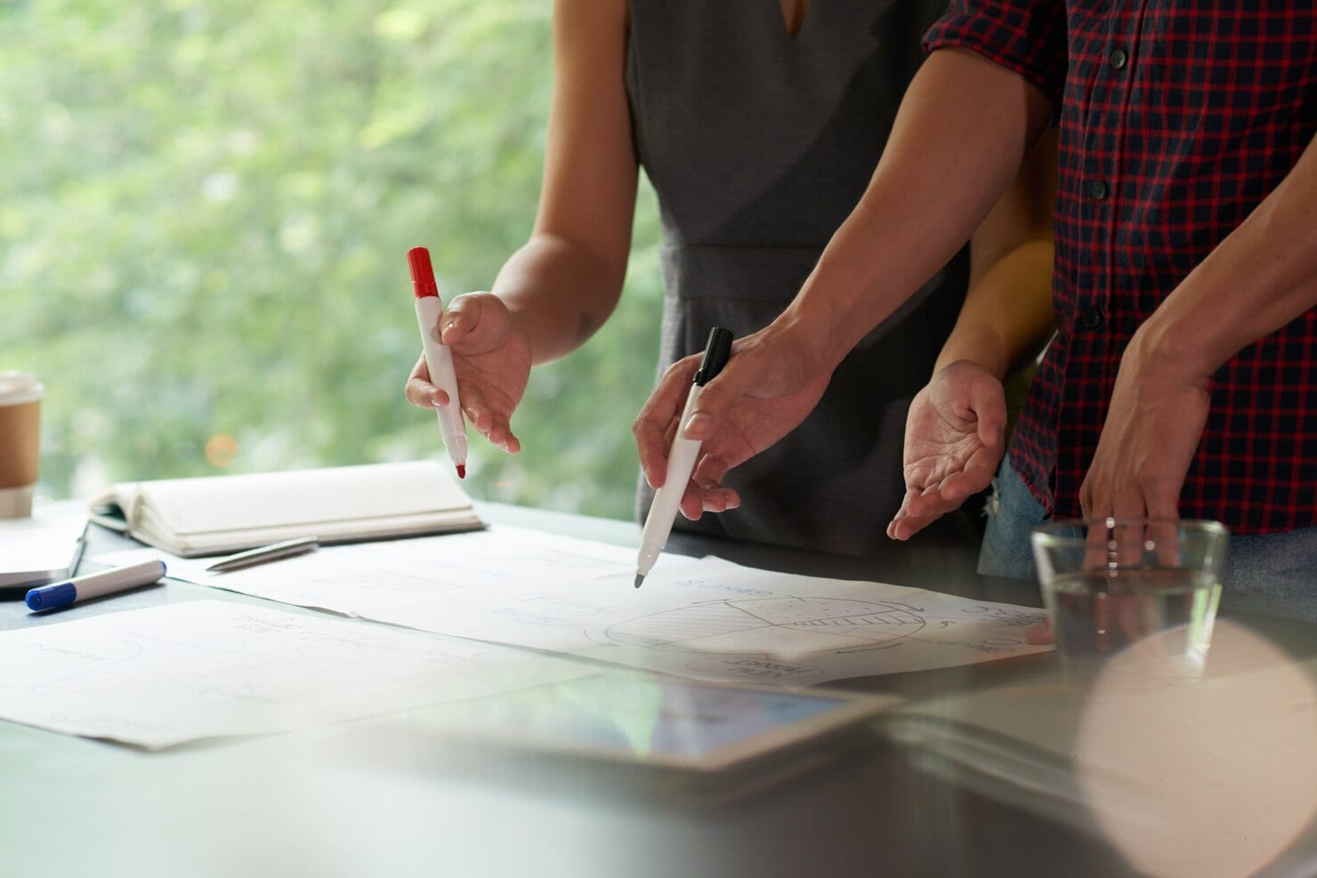 Close-up of two professionals using markers to point at printed data charts and a pie graph on a desk during a collaborative strategy meeting.