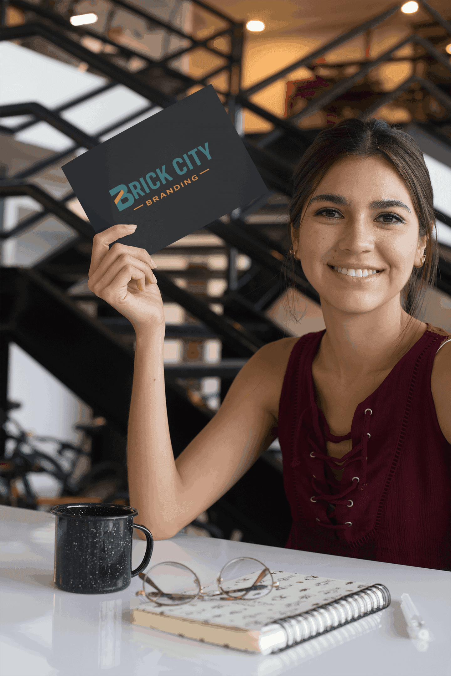 A smiling young woman in a modern office setting holding up a matte black Brick City Branding business card.