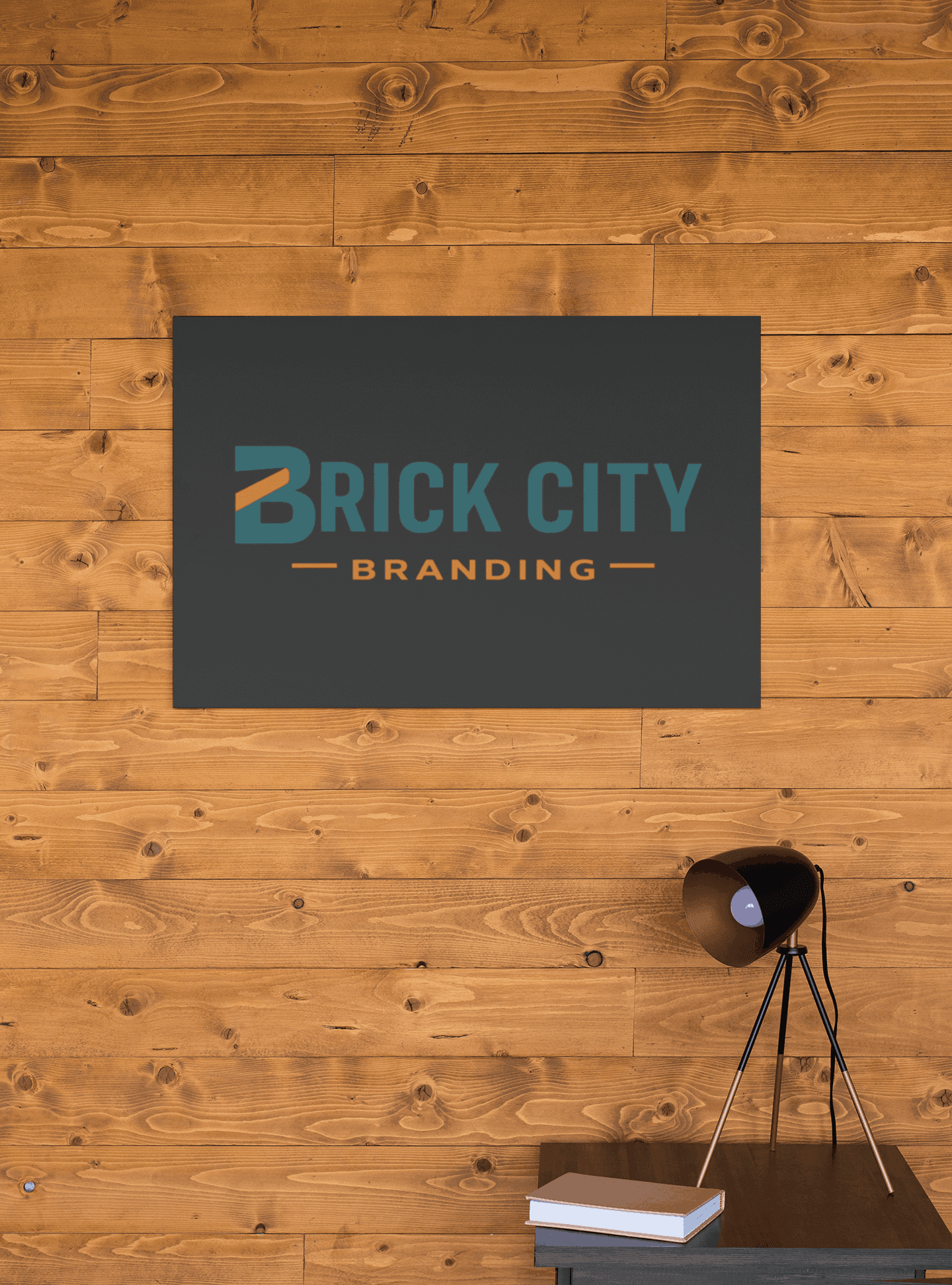 Matte charcoal grey office wall sign with teal and orange Brick City Branding logo, mounted on a horizontal light wood plank accent wall.