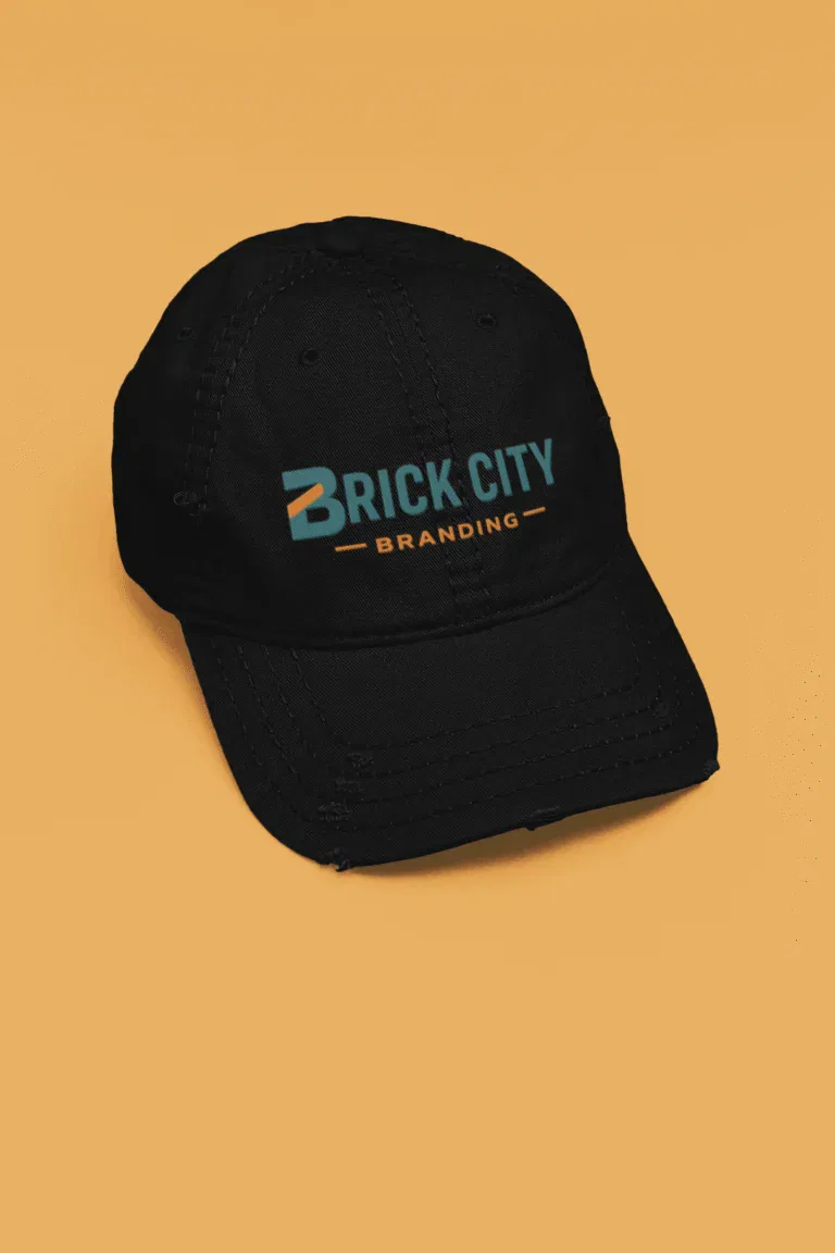 A black Otto Cap style dad hat with a slightly distressed brim, featuring the Brick City Branding logo in teal and orange, isolated on a solid yellow background.
