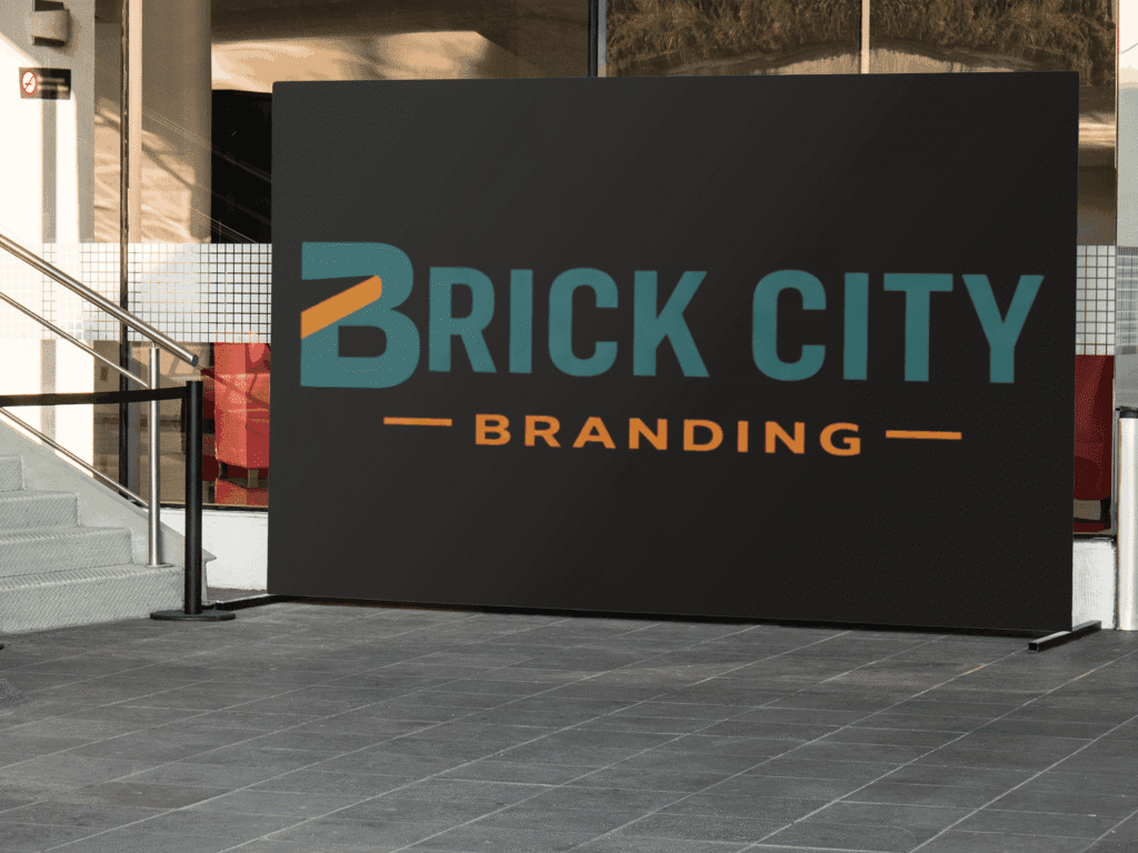 A large, matte black rectangular trade show backdrop featuring the Brick City Branding logo in teal and orange, positioned on a modern outdoor tiled plaza.