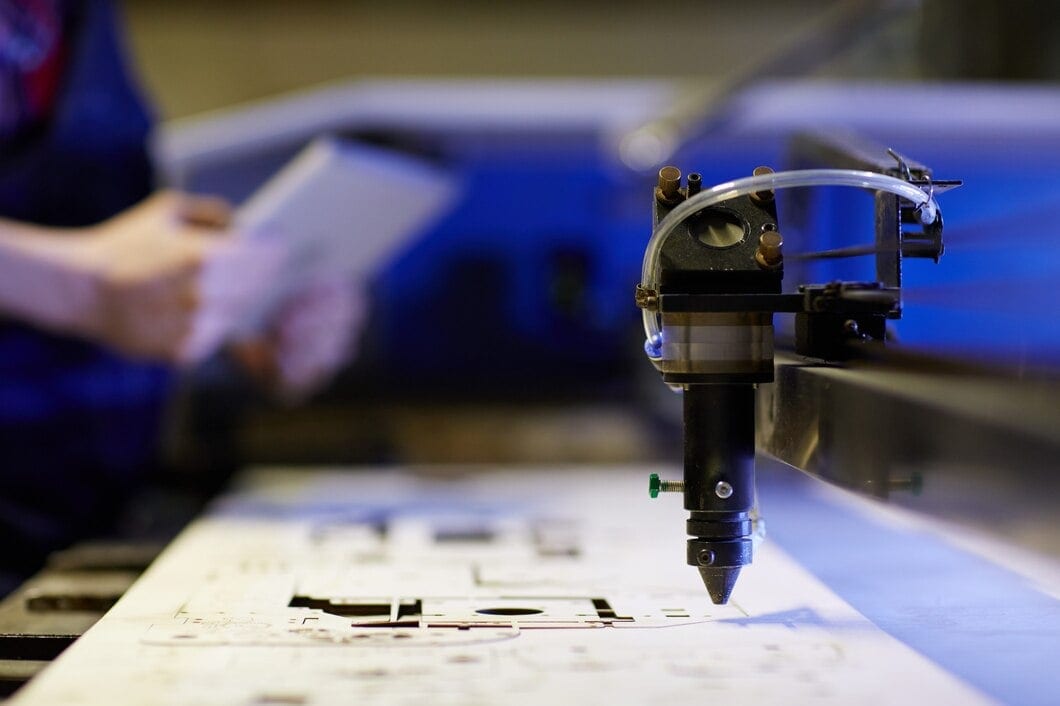 A detailed close-up of a CNC laser cutting head focused on a white material sheet, with an operator using a tablet in the background.