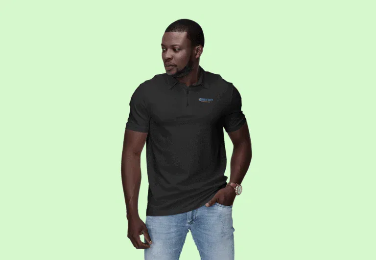 A man with a serious expression wearing a black short-sleeve polo shirt with a small Brick City Branding logo on the chest, paired with light wash denim jeans against a pale green background.