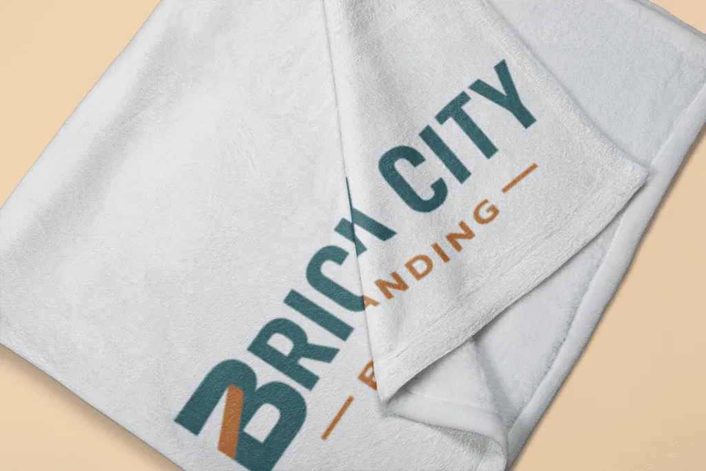 A close-up of a folded soft white fleece blanket featuring the Brick City Branding logo in teal and orange, suitable for horses or home use.